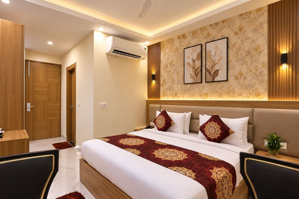 A hotel room with a bed, bedside tables, a desk, an air conditioning unit, and a wall-mounted light fixture.
