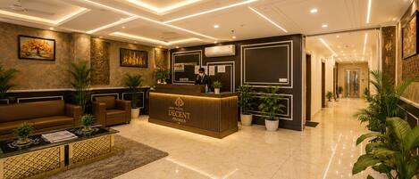 Vestíbulo de hotel con recepción, zona de estar y un pasillo que da a otras habitaciones.