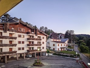 A multi-story building with balconies, a parking area, and a road in the background.