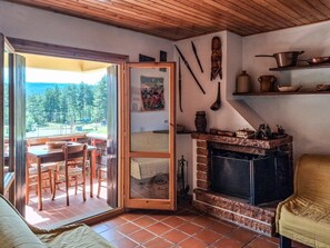 Un interior acogedor con chimenea, una zona de comedor con mesa y sillas, y vistas a una terraza exterior a través de un ventanal.