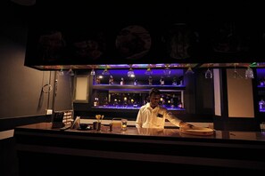 A bar area with a bartender, shelves of bottles, and a menu board. - Subra Grand - karur (Karur)