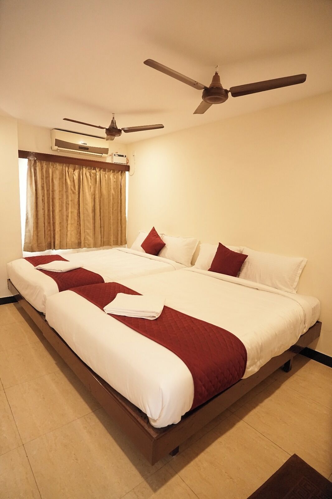 A hotel room with a large bed, two ceiling fans, a window with curtains, and an air conditioning unit.