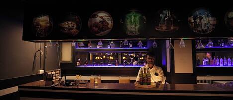 A bar area with a bartender, shelves of bottles, and a counter with glasses and a menu.