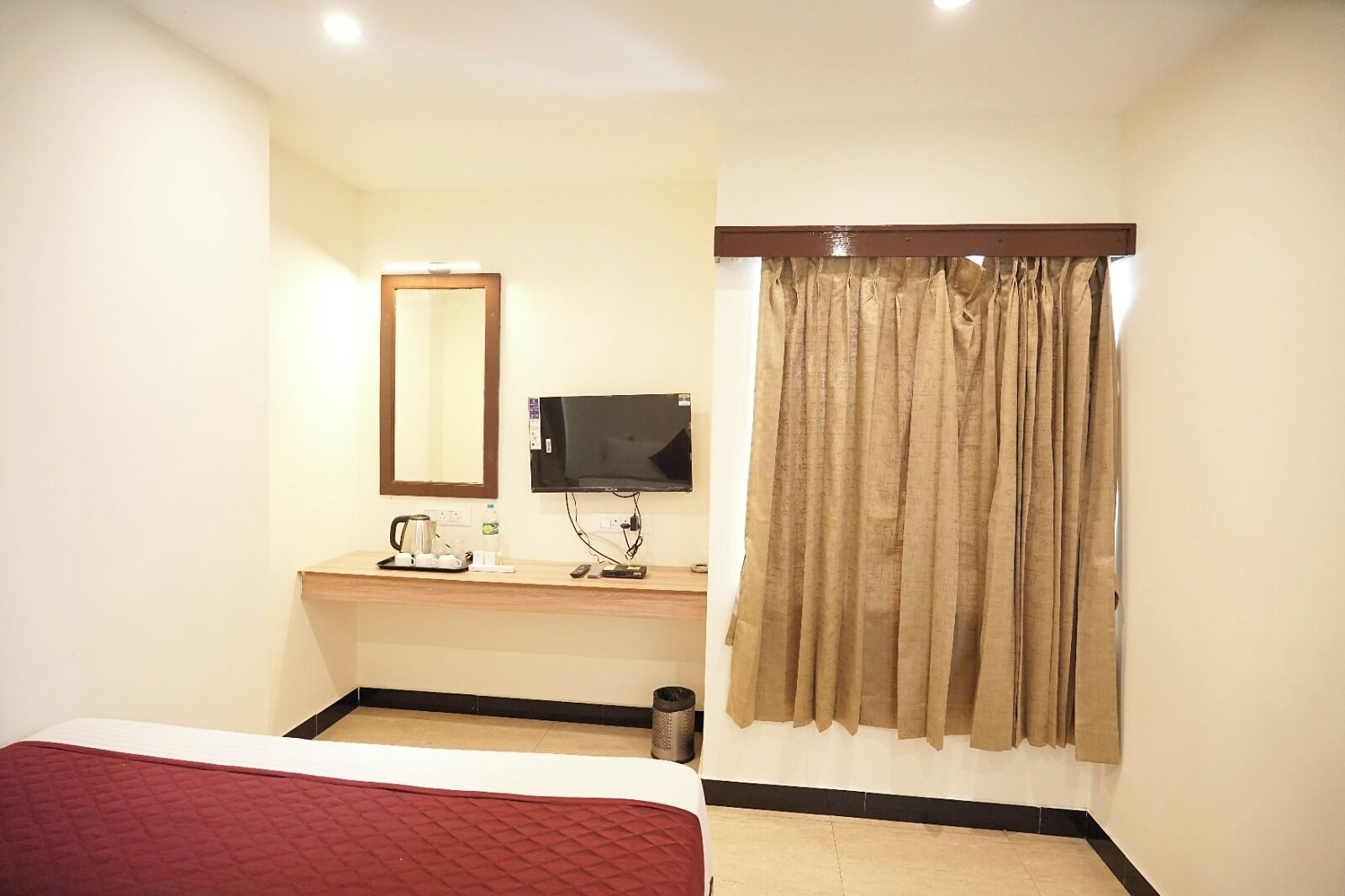 A hotel room with a bed, a desk with a television, a mirror, and a window with curtains.