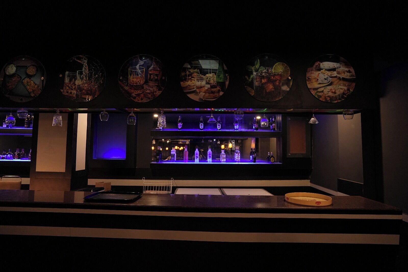 A bar area with a counter, shelves of bottles, and decorative plates above.