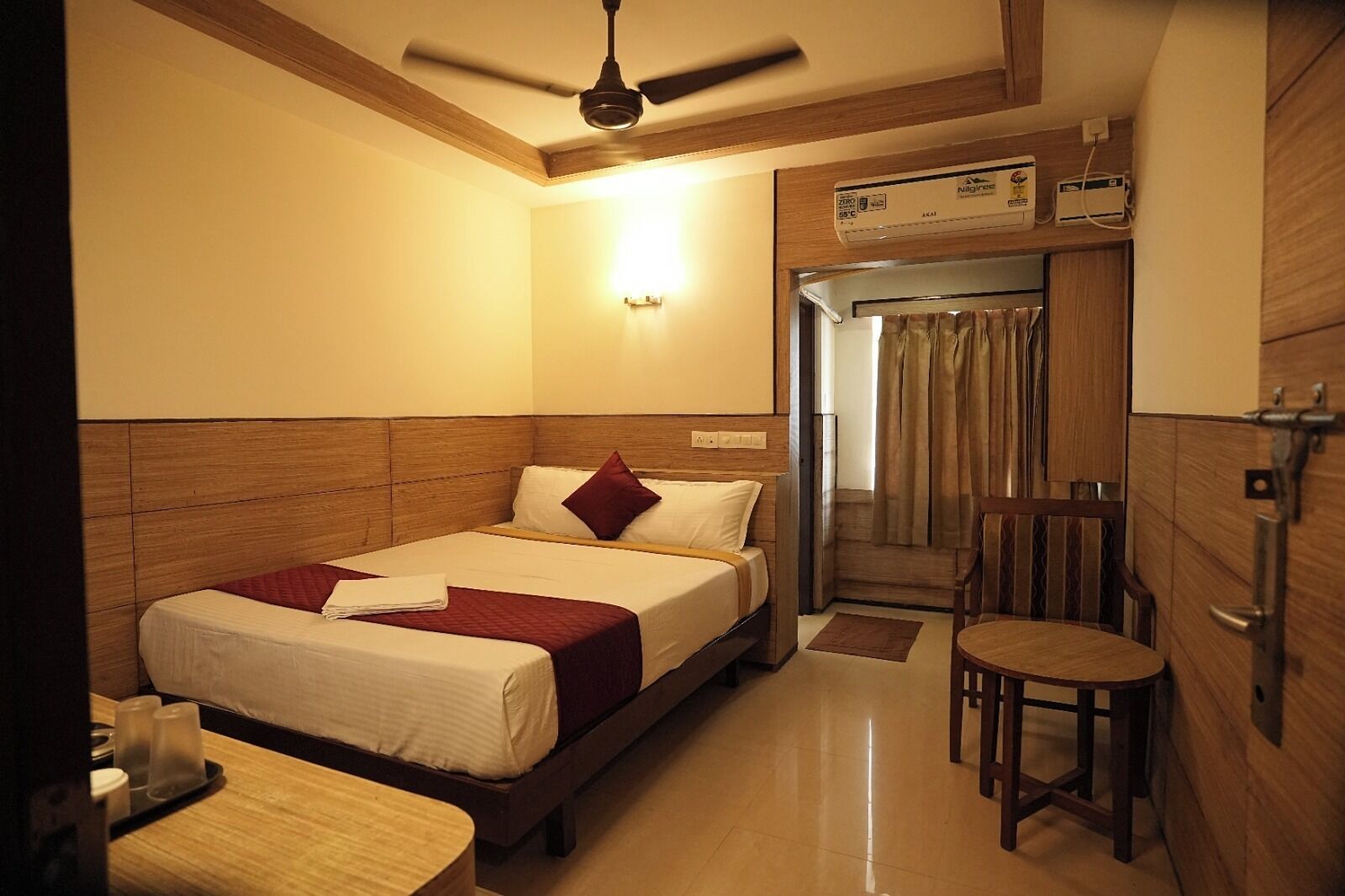 A hotel room with a bed, a chair, a ceiling fan, and a bathroom door.