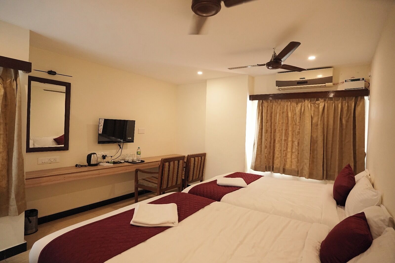 A hotel room with a bed, a desk with a TV, a ceiling fan, and an air conditioning unit.