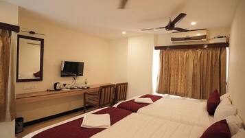 A hotel room with a bed, a desk with a TV, a ceiling fan, and an air conditioning unit.