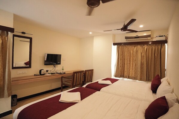 A hotel room with a bed, a desk with a TV, a ceiling fan, and an air conditioning unit. - Subra Grand - karur (Karur)