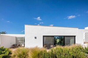 A modern building with a flat roof, large windows, and a small outdoor seating area with chairs.