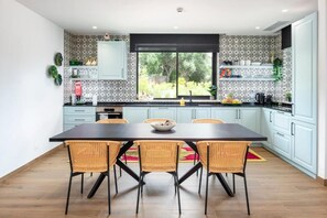 A modern kitchen with a dining table and chairs, white cabinets, and a window with a view of greenery.