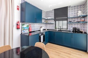 A compact kitchen with blue cabinets, a black countertop, and patterned backsplash.