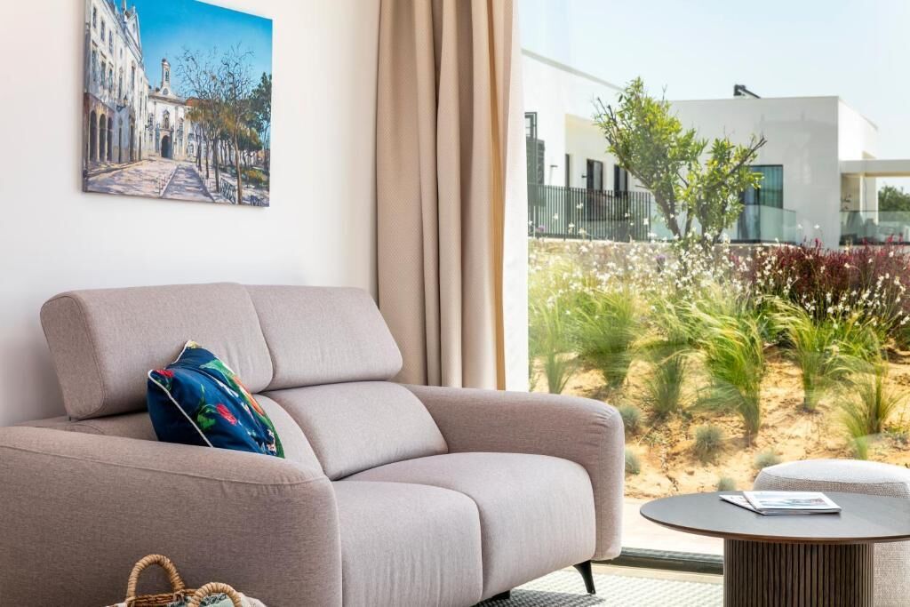 Ein modernes Wohnzimmer mit einer Couch, einem kleinen runden Tisch und Blick auf einen Garten sowie ein Gebäude.