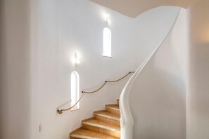 A staircase with a white wall, two small windows, and a rope railing.