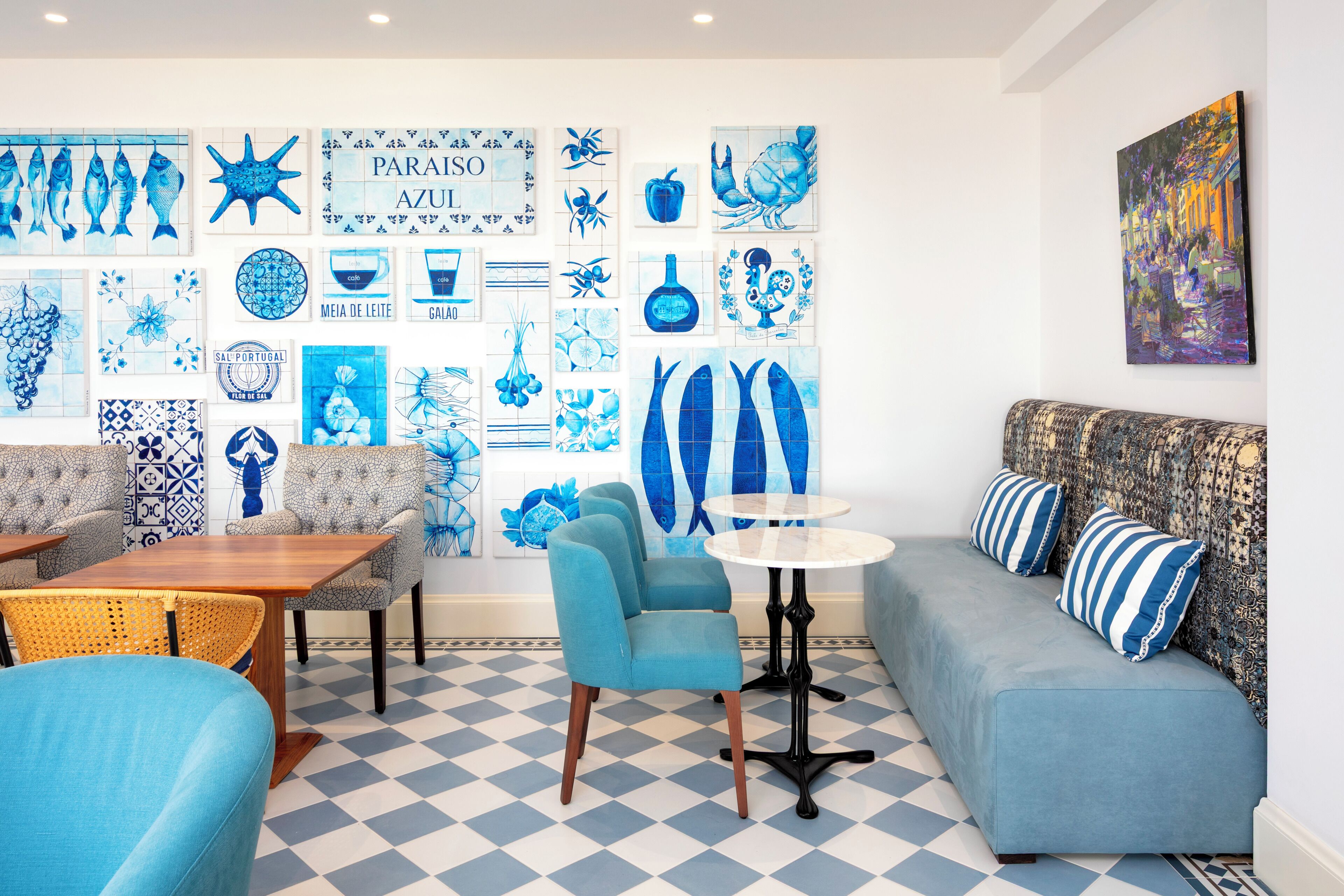 A room with a checkered floor, a sofa, a table, chairs, and a wall decorated with blue tiles featuring various designs.