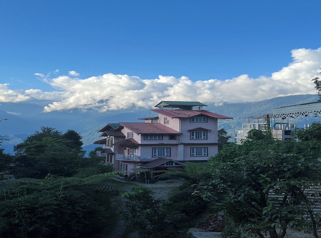 A multi-story building with a green roof, surrounded by lush greenery and mountains in the background.