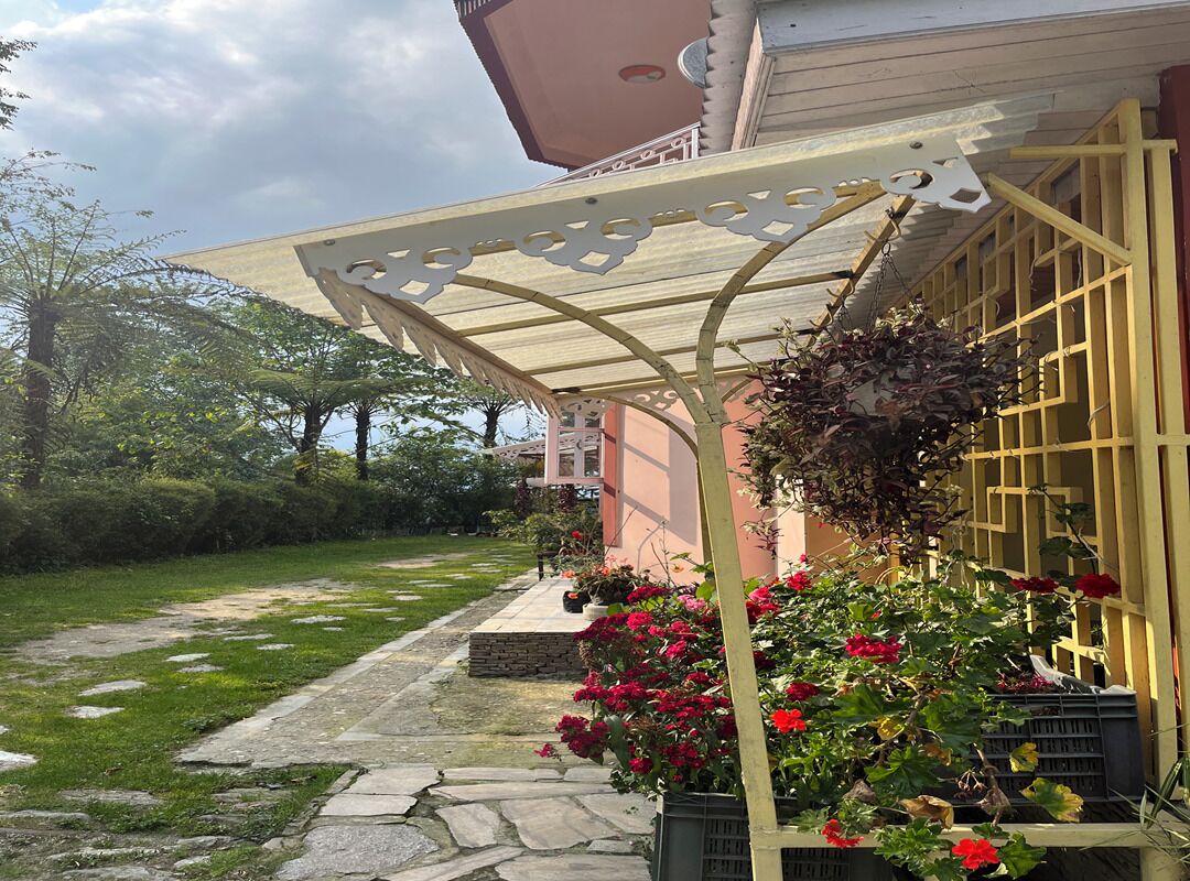 A covered outdoor area with a pergola, potted plants, and a pathway leading to a building.