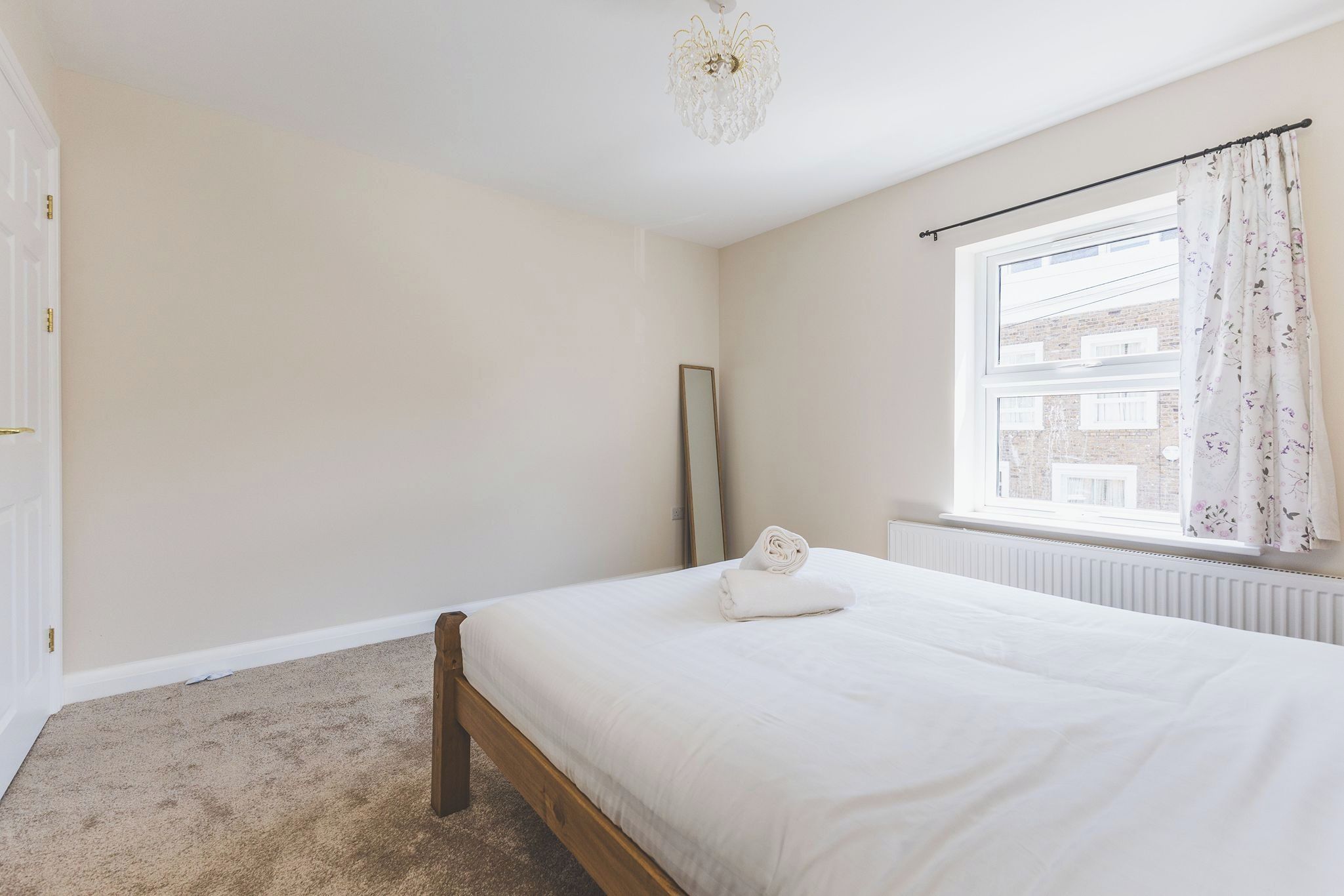 Een slaapkamer met een bed, een radiator, een raam met gordijnen en een deur.