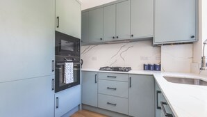 A compact kitchen with grey cabinets, a built-in oven, a gas stove, and a marble backsplash. - Modern 2BDR 2BA Oasis near Richmond and Twickenham (Greater London)