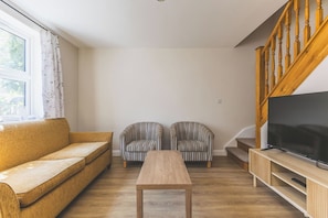 Ein Wohnzimmer mit einer Couch, zwei gestreiften Sesseln, einem Couchtisch, einem Fernseher auf einem Holzschrank und einer Treppe.