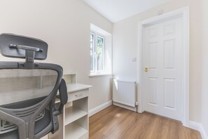 Ein Zimmer mit weißem Schreibtisch, einem Stuhl, einem Heizkörper und einer weißen Tür.