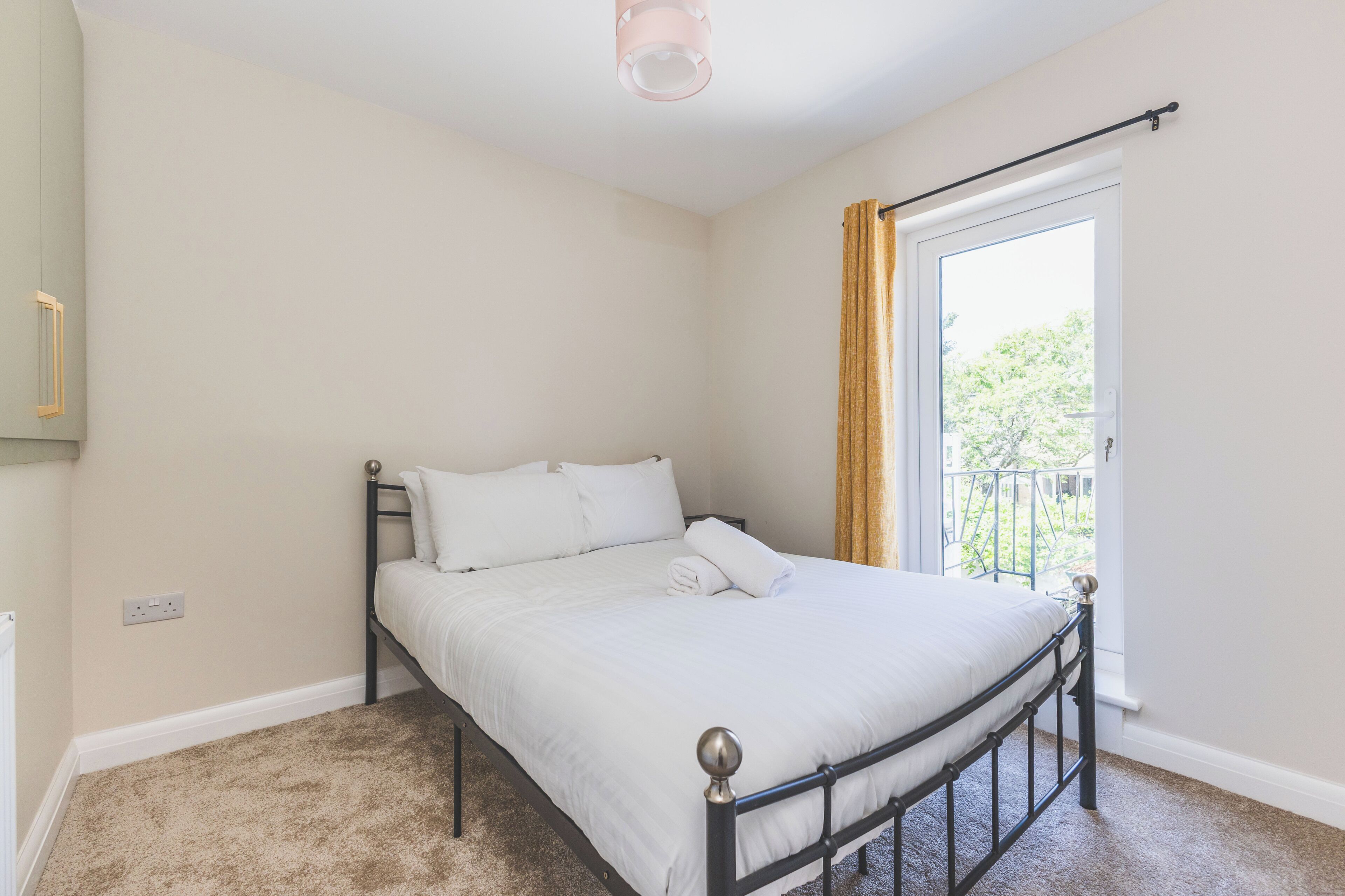 A single bed with a metal frame and white bedding in a room with beige walls and a carpeted floor.