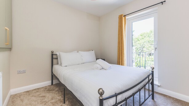 A single bed with a metal frame and white bedding in a room with beige walls and a carpeted floor. - Modern 2BDR 2BA Oasis near Richmond and Twickenham (Greater London)
