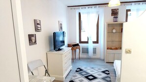 A living room with a sofa, a TV, a small table, and a patterned rug. - A charming studio on the French Riviera, 25 minutes from Nice, nestled between the sea and the mountains. (L'Escarène)