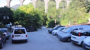 A parking lot with several cars, a bridge in the background, and trees. - A charming studio on the French Riviera, 25 minutes from Nice, nestled between the sea and the mountains. (L'Escarène)