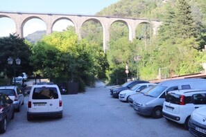 Ein Parkplatz mit mehreren Autos, im Hintergrund eine Brücke und Bäume.