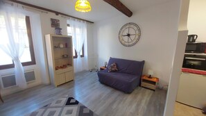 Ein Zimmer mit einer Couch, einer Uhr, einem Bücherregal und einer Küchenzeile.