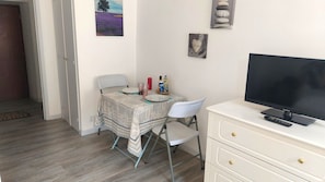 Ein kleiner Raum mit Esstisch, Stühlen, Fernseher und Schrank.