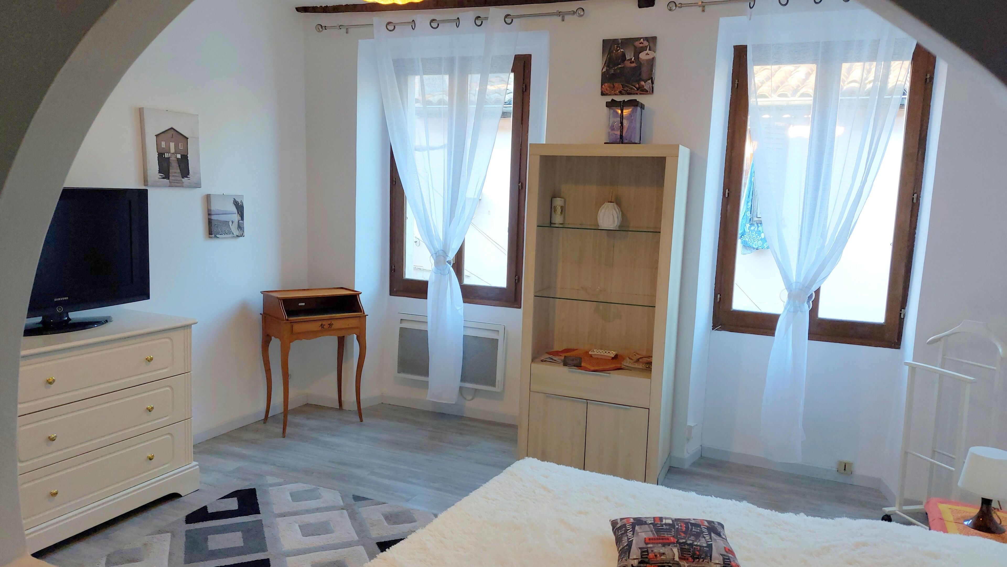 Un dormitorio con cama, televisión, mueble de madera y ventana con cortinas.