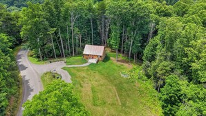 Eine Holzhütte, umgeben von dichtem Wald, mit einer kurvenreichen Straße, die dorthin führt.