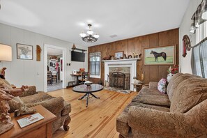 A living room with a fireplace, wooden flooring, and patterned furniture. - Escape to this spacious countryside retreat featuring beautiful mountain views, a wraparound porch. (Galax)