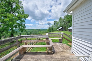 A wooden deck with a picnic table, surrounded by a white building and a view of a forested landscape. - Escape to this spacious countryside retreat featuring beautiful mountain views, a wraparound porch. (Galax)