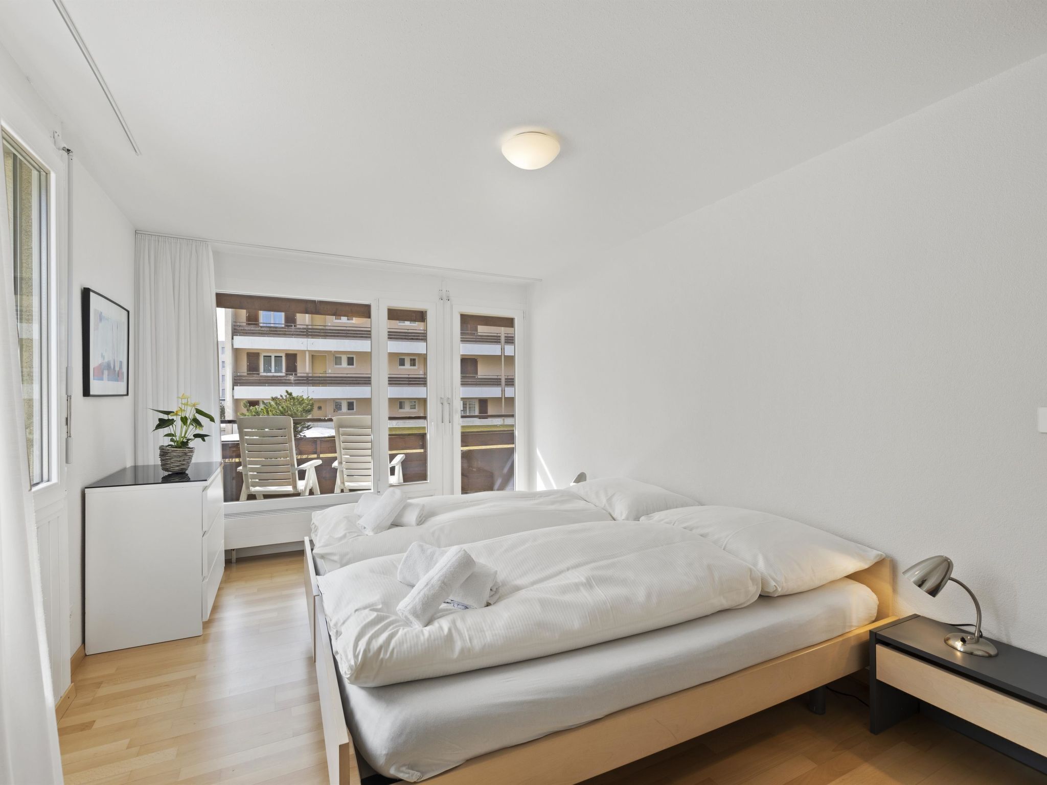 A bedroom with a bed, bedside table, lamp, and a view of an outdoor balcony.