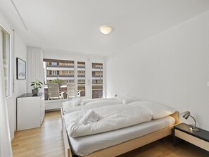 Ein Schlafzimmer mit Bett, Nachttisch, Lampe und Blick auf einen Balkon.