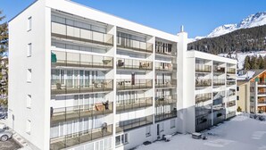 Ein mehrstöckiges Hotel mit Balkonen, einem Parkplatz und einem verschneiten Berg im Hintergrund.