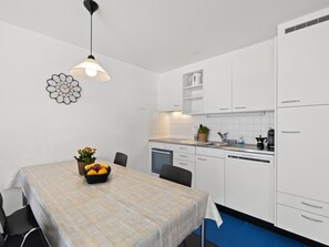 Una cocina moderna con armarios blancos, una mesa de comedor con fruteros, y una lámpara colgante.