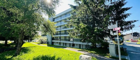 A modern building with a multi-story structure, a grassy area with rocks, and a clear sky.