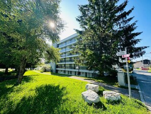 Un edificio moderno con una estructura de varios pisos, un área verde con rocas y un cielo despejado.