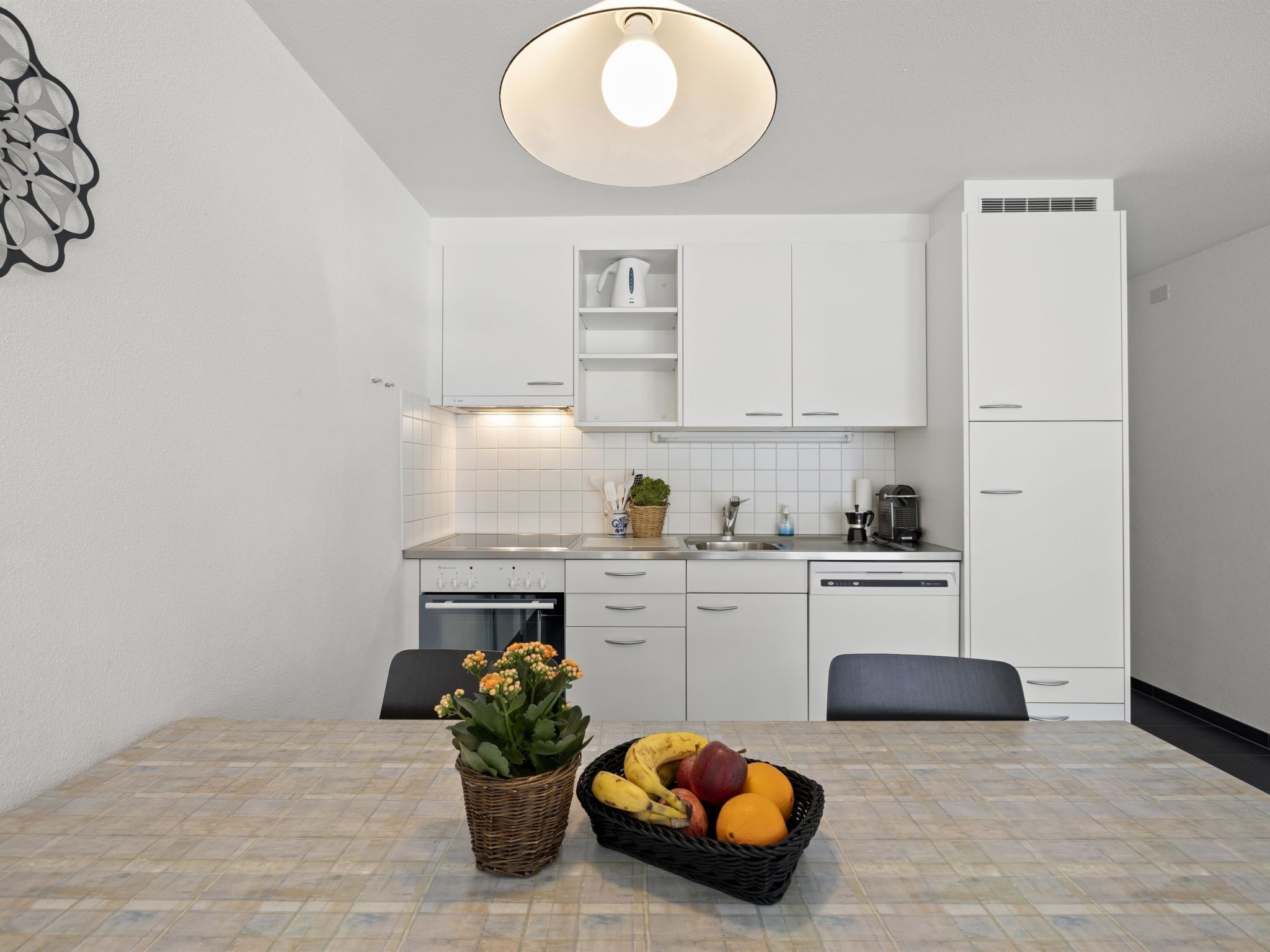 Een moderne keuken met witte kasten, een inbouwoven en een eethoek met een tafel gedekt voor twee personen.