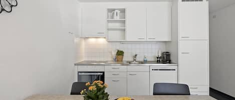 Een moderne keuken met witte kasten, een inbouwoven en een eethoek met een tafel gedekt voor twee personen.