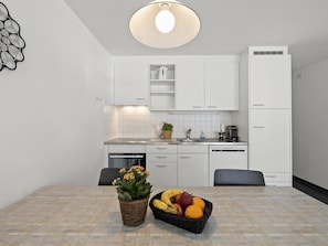 Une cuisine moderne avec des meubles blancs, un four encastré et un coin repas avec une table dressée pour deux personnes.