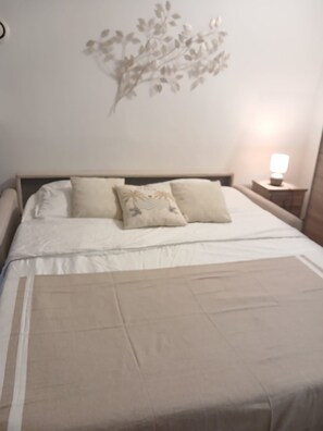 Ein ordentlich bezogenes Bett mit weißer und beiger Bettdecke, zwei Kissen und einem Nachttisch mit Lampe.