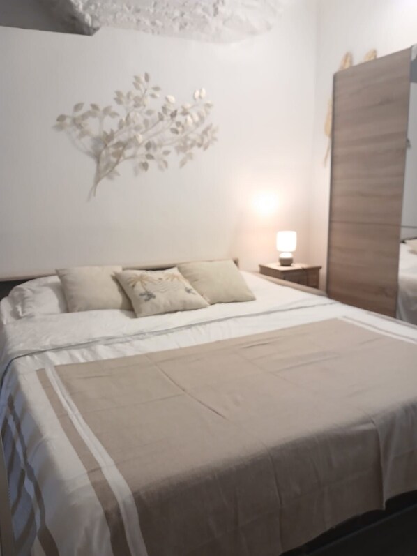 Un dormitorio con una cama, almohadas, una mesita de noche, una obra de arte en la pared y un armario de madera.