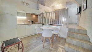 A modern kitchen with white cabinets, a dining table with chairs, and a staircase leading to an upper level. - L'Eden - Unique and Charming - Suquet (Cannes)