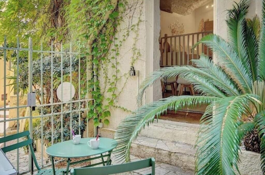 An outdoor seating area with a table and chairs, surrounded by greenery and a metal fence.