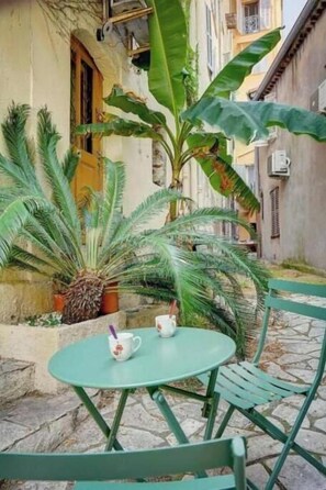 Un patio al aire libre con una mesa redonda y sillas, rodeado de plantas en macetas y la fachada de un edificio.